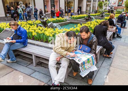 New York City,NYC NY Midtown,Manhattan,5th Fifth Avenue,Rockefeller Center,Plaza,panca,visitatore,uomo ispanico uomini maschio adulti,mappa di lettura,daffodil Foto Stock