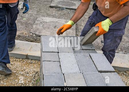 Due maestri stanno mettendo nuovi mattoni di cemento per il marciapiede. I mattoni sono stati preparati per l'installazione di un nuovo percorso pedonale. Foto Stock