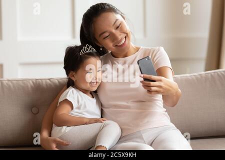 Sorridente bella mummia asiatica prendendo selfie girato con figlia bambino. Foto Stock