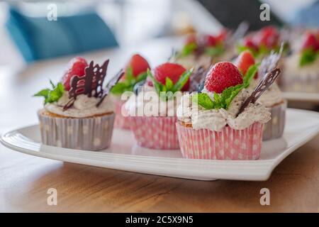 Bellissimo e colorato gruppo di cupcake decorato con bianco panna frusta, fragole, mirtilli, cioccolato e menta su tavolo di legno. Foto Stock