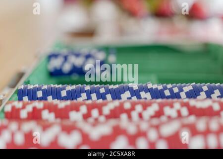 Fuoco selezionato alle file di chip di plastica blu del poker nella scatola di poker impostata su tavolo di legno e sfocare sfondo di quelli rossi. Foto Stock