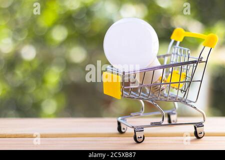 Lampadina in mini carrello contro sfondo verde naturale sfocato. Concetto di risparmio energetico e ambientale. Foto Stock