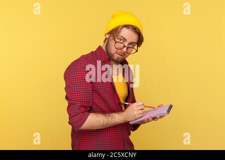 Hipster nerd ragazzo in berretto e occhiali guardando la fotocamera curioso pensieroso, scrivendo idea creativa in notebook, disegno schizzo o prendendo appunti i Foto Stock