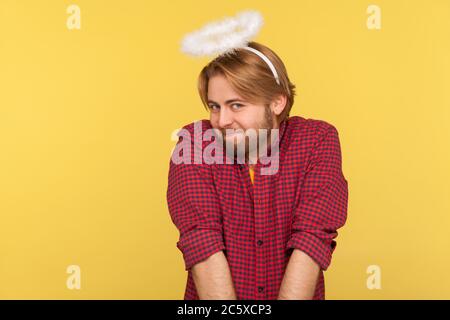 Simpatico simpatico ragazzo bearded modesto con saint nimbus sopra la testa guardando la macchina fotografica con timida espressione, presendendo angelo, concetto di comportamento obbediente. In Foto Stock