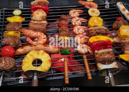 Primo piano su una griglia barbecue con gamberi, ananas, carne e verdure. Cibo artificiale fatto da cera. Vetrina, ristorante menu esempio di cibo. Foto Stock