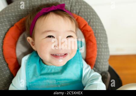 Adorabile bambina sorridente che indossa la fascia si siede in seggiolone a. casa Foto Stock