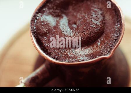 Caffè naturale con spessa schiuma, preparato in rame cezve in modo classico, su sfondo ligneo, macro foto. Foto Stock
