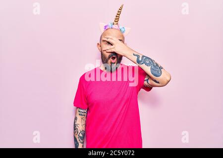 Giovane bell'uomo che indossa diadem unicorno sbirciando in shock coprendo faccia e occhi con la mano, guardando attraverso le dita paura Foto Stock