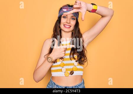 Giovane bella donna hippie con occhi blu indossando accessori e occhiali da sole sorridente rendendo cornice con mani e dita con volto felice. Creatività Foto Stock