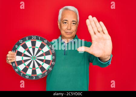 Medio età anziano uomo con capelli grigi che tiene la concorrenza bersaglio della tavola da disegno su sfondo rosso con mano aperta facendo segno di stop con serio e sicuro Foto Stock