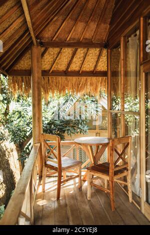 Terrazza in legno con tetto di paglia in stile balinese. Due sedie e tavolo sul balcone. Foto Stock