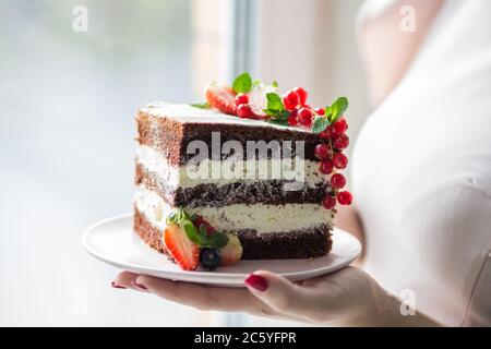 Fetta di pan di Spagna al cioccolato su un piatto bianco con panna e bacche. Foto Stock