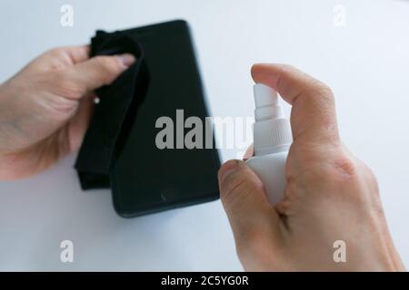 La mano della donna sta spruzzando alcol, disinfettante spray sul telefono cellulare, prevenire l'infezione del virus Covid-19, la contaminazione di germi o batteri, pulire o pulire il telefono per eliminare, scoppio di Coronavirus Foto Stock