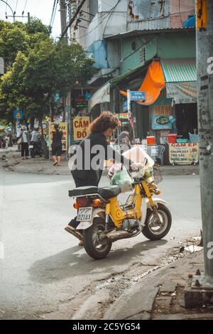 Saigon, Vietnam - 4 luglio 2020: Le strade di Saigon (ho Chi min City), una donna che spinge una piccola moto gialla, è la città più popolosa di Viet Foto Stock