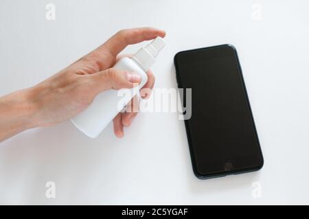 La mano della donna sta spruzzando alcol, disinfettante spray sul telefono cellulare, prevenire l'infezione del virus Covid-19, la contaminazione di germi o batteri, pulire o pulire il telefono per eliminare, scoppio di Coronavirus Foto Stock