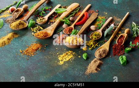 Varie spezie ed erbe secche su sfondo verde scuro. Vista dall'alto delle spezie in cucchiai di legno Foto Stock