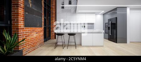 Panorama di cucina in stile loft con pareti in mattoni, mobili bianchi e grandi finestre Foto Stock