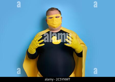 giovane uomo caucasico grasso pulizia in costume di supereroe e in maschera, è pronto a salvare il pianeta da sporcizia. isolato su sfondo blu Foto Stock