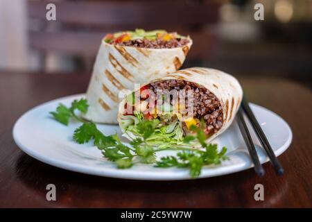 Burrito vegano. Affettato su un piatto di cibo crudo con ingredienti vegani. Primo piano Foto Stock