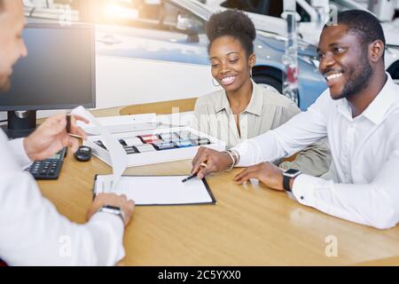 giovane agente di vendita professionale caucasico e clienti afro-americani hanno una conversazione amichevole in concessionaria, i clienti sono venuti a comprare una nuova auto Foto Stock