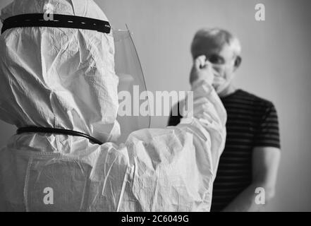 Immagine del medico che misura la febbre dell'uomo anziano con termometro a infrarossi senza contatto. Istantanea bianca e nera della visita del medico a casa del paziente durante la quarantena. Concetto di Covid-19 Foto Stock