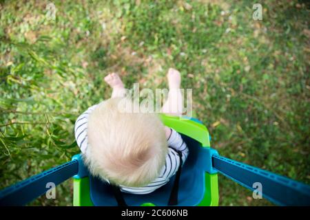 Un ragazzo piccolo che si diverte a giocare su un'altalena sotto un albero in un giardino Foto Stock