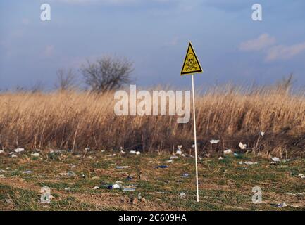 Triangolo giallo con simbolo cranio e crossone sul territorio abbandonato con spazzatura. Campo rifiuti con segnale di pericolo tossico. Concetto di ecologia, inquinamento ambientale e pericolo. Foto Stock