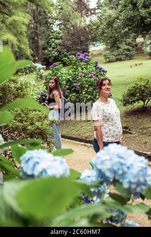 Coppia di amici che si posano su un giardino fiorente in primavera. Uno di loro è incinta Foto Stock
