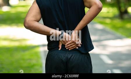 Giovane sportivo nero che soffre di dolore alla schiena durante l'allenamento al parco, primo piano Foto Stock