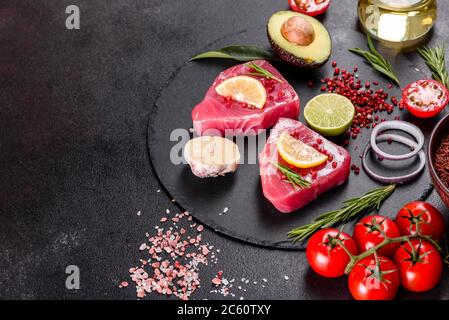 Bistecche di filetto di tonno fresco con spezie ed erbe su fondo nero. Preparare il tonno per la cottura Foto Stock