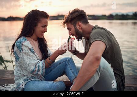 giovane donna che alimenta l'uomo con una fetta di anguria al mare Foto Stock