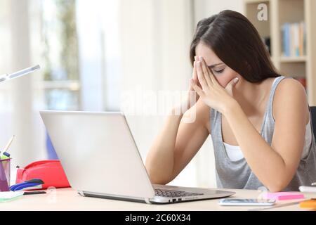 Donna studentesca stanca con un computer portatile che si lamenta seduto su una scrivania nel soggiorno di casa Foto Stock