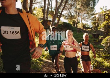 Gruppo multietnico di atleti che corrono su sentieri di montagna. Uomini e donne che corrono in gara di campionato di maratona di fondo. Foto Stock