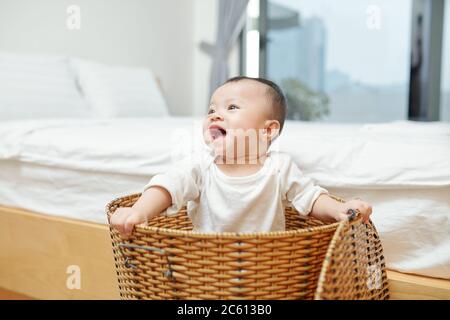 Adorabile ragazza asiatica che gioca in vimini cesto di bucato in camera da letto Foto Stock