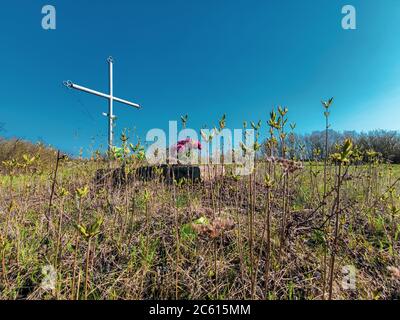 Tomba a croce invecchiata con fiori e erba adulta. svegliare la vecchia tradizione cristiana Foto Stock