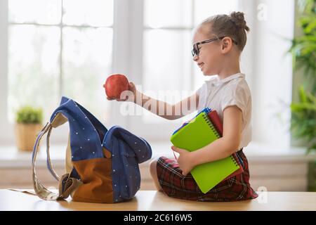 Bambino felice che si prepara per la scuola. La bambina sta mettendo le cose nello zaino. Foto Stock