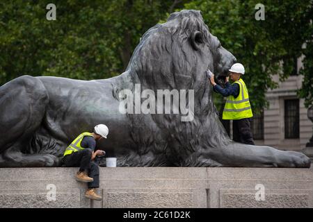 I lavoratori puliscono e lucidano una delle quattro statue di leoni alla base della colonna di Nelson, in Trafalgar Square, Londra. Foto Stock