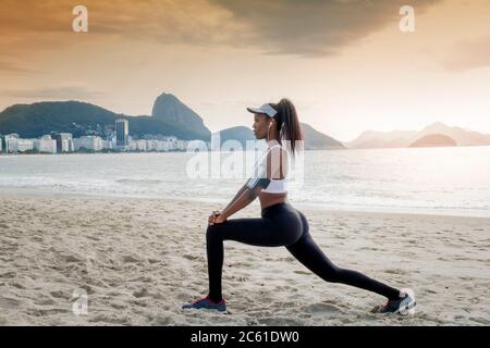 America del Sud, Brasile, spiaggia di Copacabana. Una donna brasiliana nera nei suoi primi anni trenta che si allunga prima di una corsa Foto Stock