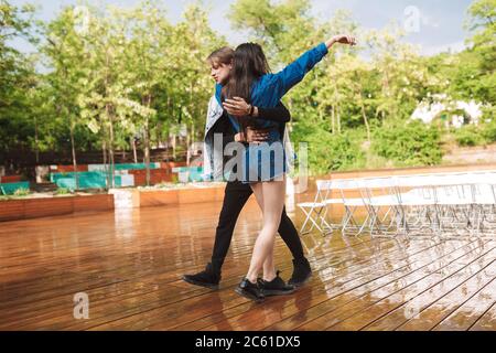 Bella coppia che balla felicemente e che si agguda sotto la pioggia in data nel parco Foto Stock