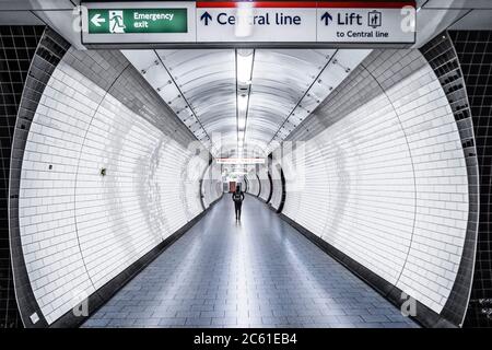 Una donna che cammina lungo un passaggio vuoto in una stazione sulla Central Line del sistema metropolitano di Londra Foto Stock