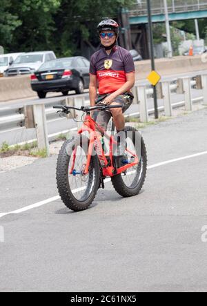 Un ciclista americano asiatico guida la sua mountain bike senza mani sul manubrio. Vicino al Bayside Marina & Cross Island Parkway a Queens, New York. Foto Stock