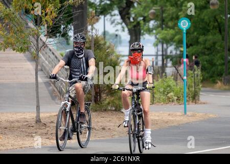 Una coppia in bicicletta su un sentiero vicino alla Marina di Bayside. Uno indossa una bandana e l'altro una sciarpa per il viso. A Bayside, Queens, New York City. Foto Stock