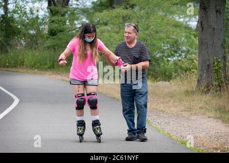 Un uomo di mezza età insegna a una giovane ragazza - probabilmente famiglia - come rollerblade. Vicino al Bayside Marina a Queens, New York City. Foto Stock