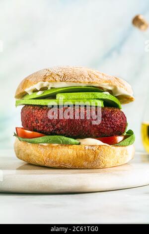 hamburger vegano senza carne con avocado, pomodori e spinaci sul tavolo e vino rosso in un bicchiere Foto Stock