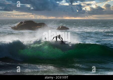 Surfer sulla cresta dell'onda, guardando dalla spiaggia di Reñaca, costa centrale del Cile. Sullo sfondo, una nave che arriva al porto di Valparaiso Foto Stock