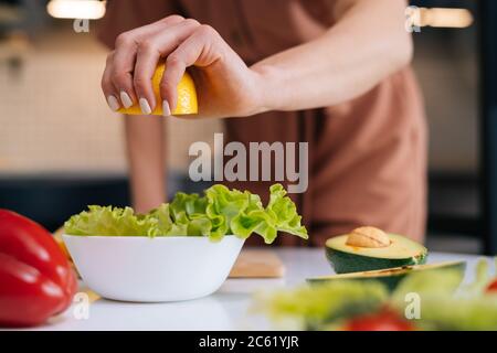 Primo piano delle mani delle donne che spremono il succo dal limone nel recipiente per insalate. Foto Stock