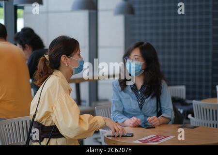 Giovani donne che parlano in cafè, indossando maschera chirurgica per prevenire l'infezione di coronavirus COVID-19 polmonite Foto Stock