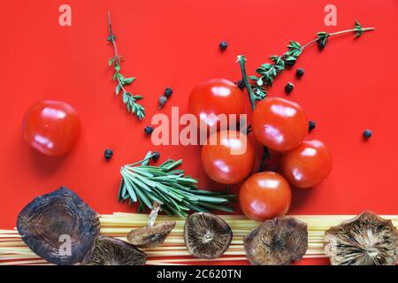 Spaghetti, funghi selvatici, pomodori con un rametto di timo e rosmarino su fondo rosso Foto Stock