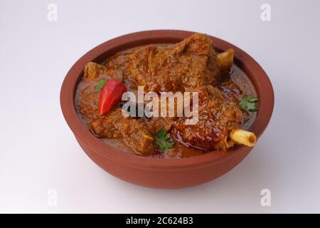 Curry di montone o curry di agnello, piatto piccante e delizioso guarnito con foglie di coriandolo, peperoncino rosso e spezie all'anice stellato in una ciotola di terracotta con bianco Foto Stock