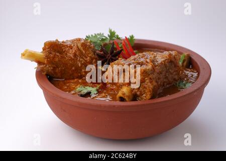 Curry di montone o curry di agnello, piatto piccante e delizioso guarnito con foglie di coriandolo, peperoncino rosso e spezie all'anice stellato in una ciotola di terracotta con bianco Foto Stock